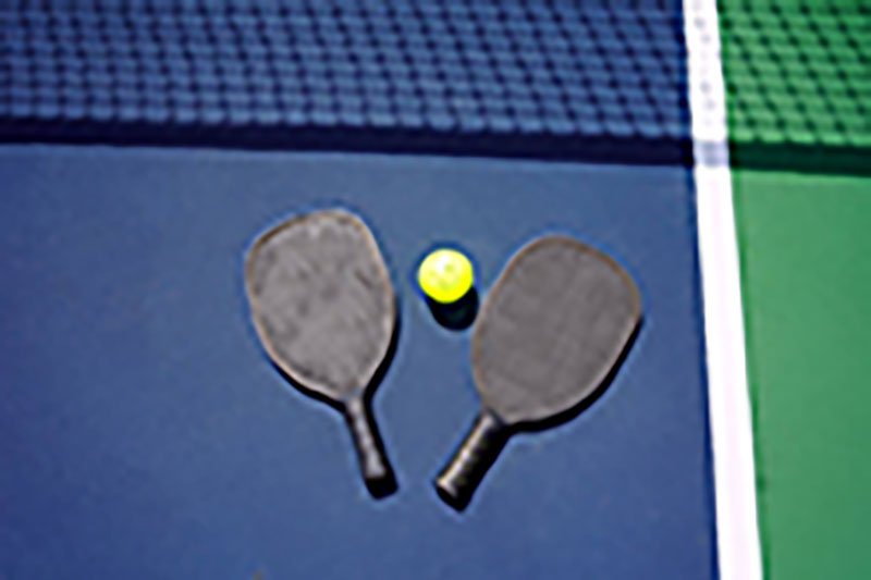 Dual Matte Paddles and Ball two matte black pickleball paddles with a yellow ball on a blue court