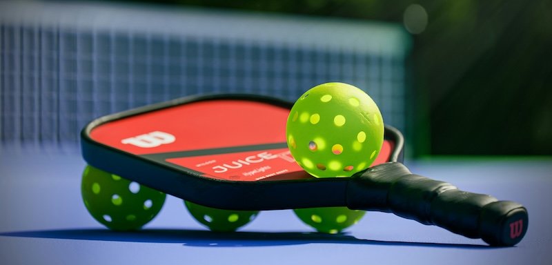 pickleball-paddle-and-balls A red pickleball paddle with green pickleball balls on a court