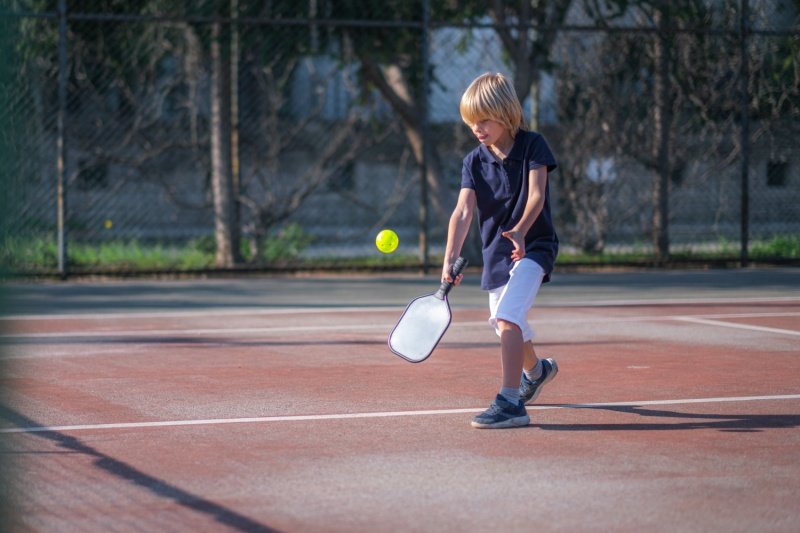 Young boy playing pickleball on an outdoor court, preparing to hit a yellow ball