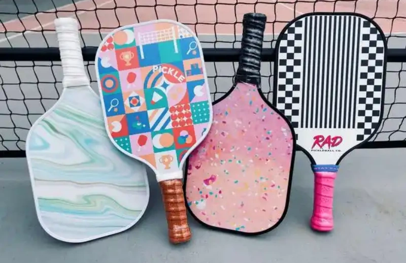 Four uniquely designed pickleball paddles with colorful patterns placed near a net
