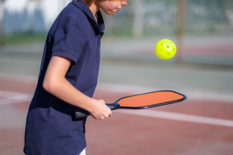Close-up of a young player practicing pickleball with an orange paddle and yellow ball