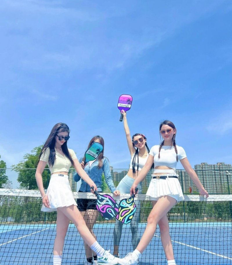 Group enjoying pickleball with vibrant paddles and a clear blue sky Four women posing with colorful pickleball paddles on an outdoor court under a sunny sky