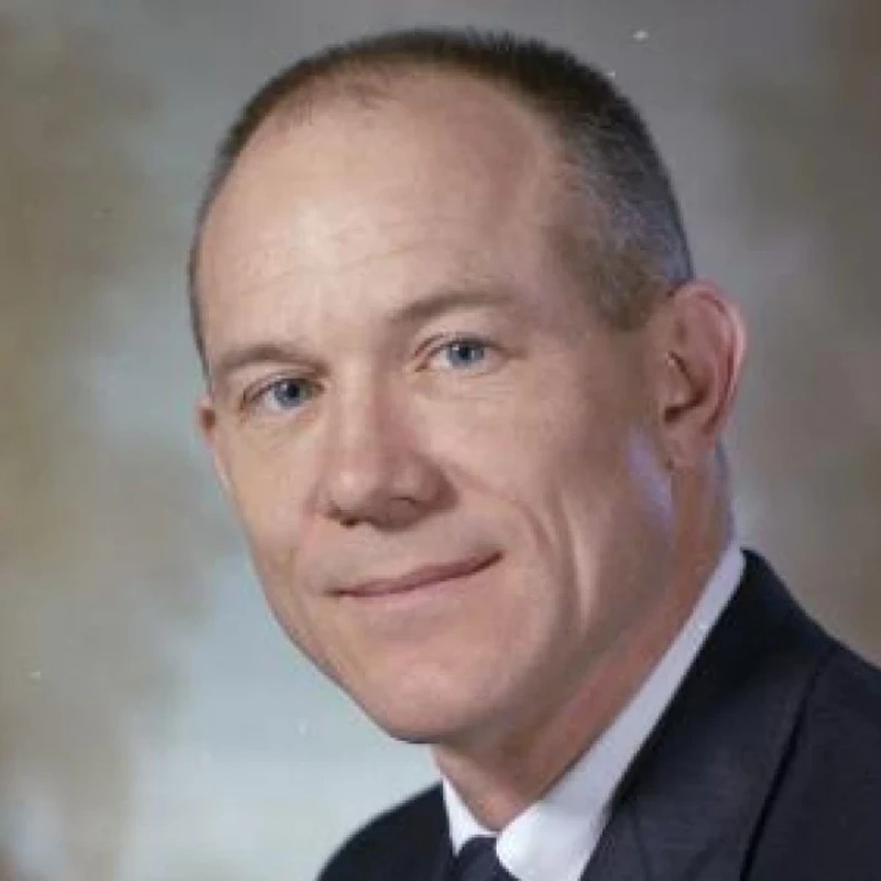 Portrait of a professional man in formal attire with a neutral background.