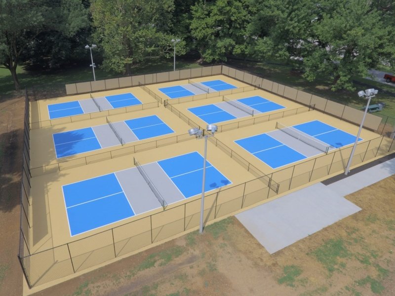 Outdoor pickleball court complex with multiple playing surfaces Multiple blue pickleball courts in an outdoor facility surrounded by fencing