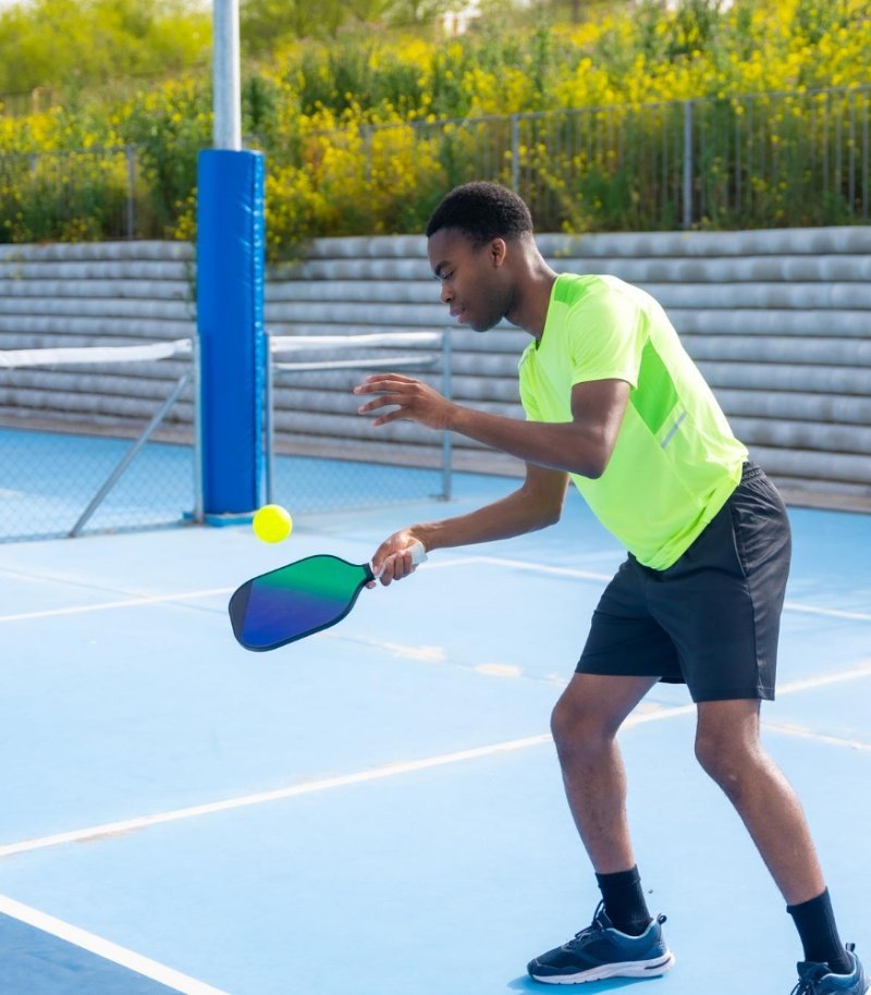 Player in bright sportswear practicing pickleball on an outdoor court