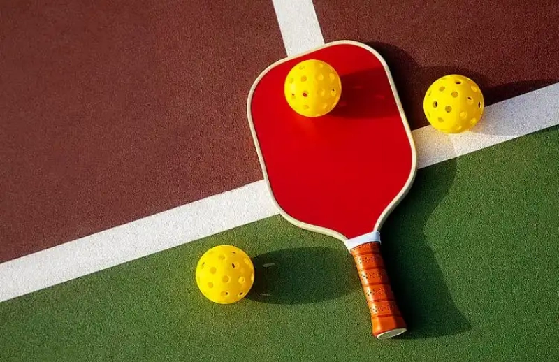 Red pickleball paddle with yellow balls on a colorful court intersection