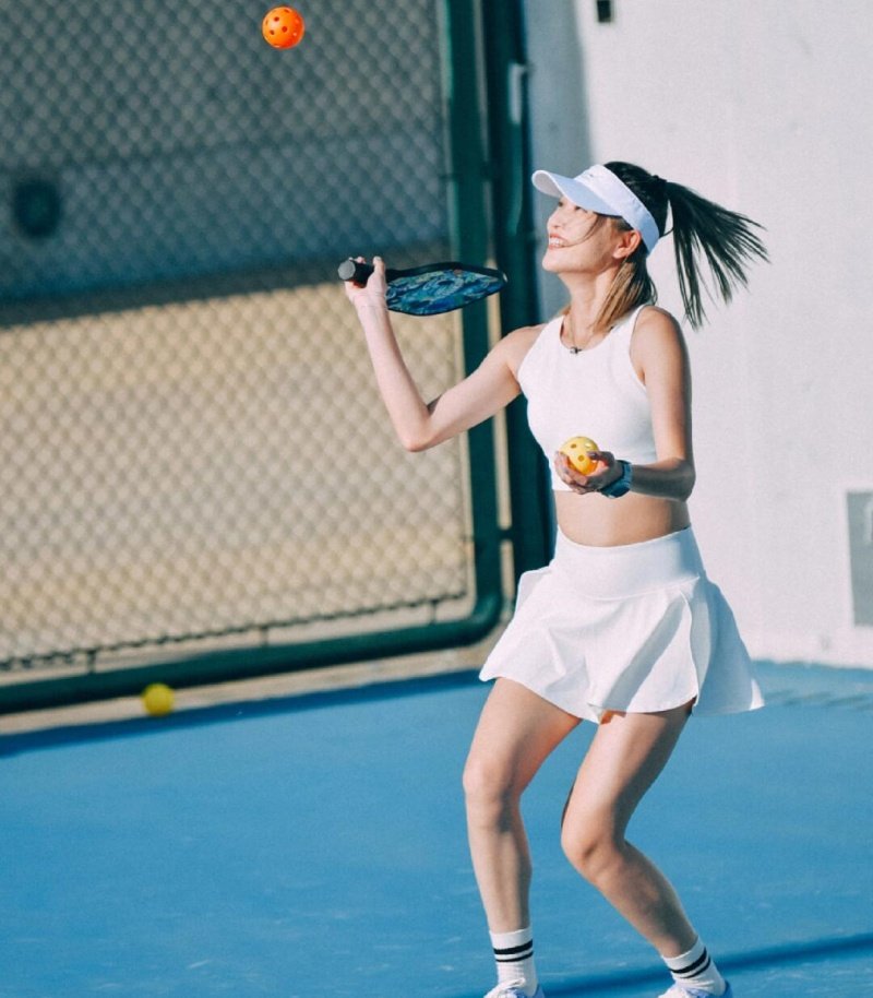 Female player juggling pickleballs with a paddle on an outdoor court
