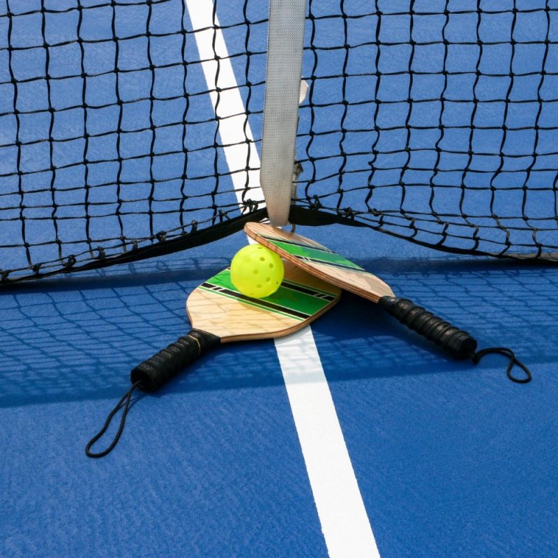 Two wooden pickleball paddles with a yellow ball resting near a net on a blue court.