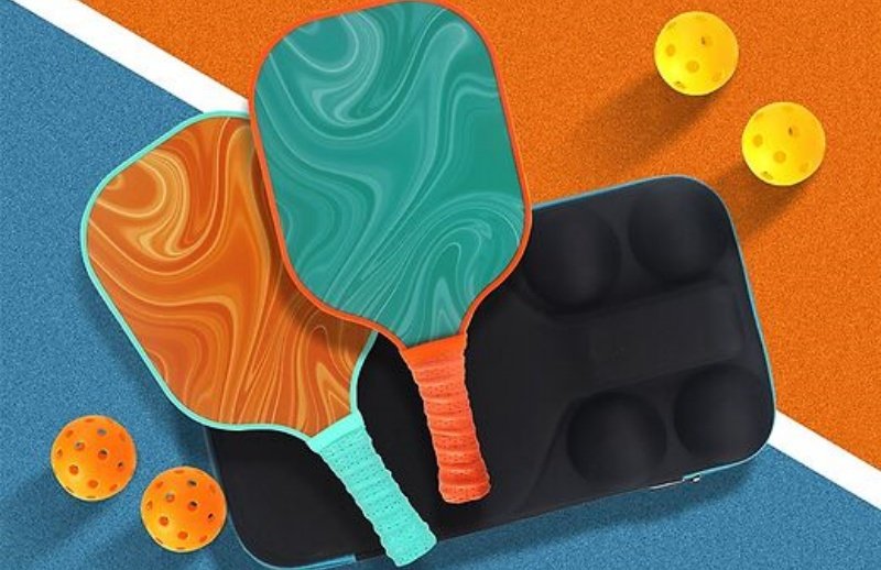 Swirl-patterned pickleball paddles with vibrant grips and yellow balls on a colorful court