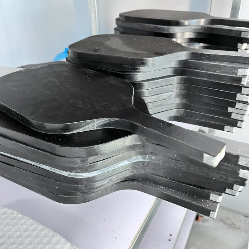Unfinished pickleball paddles in production Stack of unfinished black pickleball paddles in production