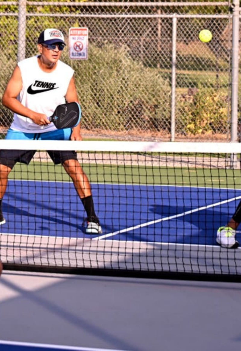 intense pickleball match pickleball players at net, with ball in the air and fence background
