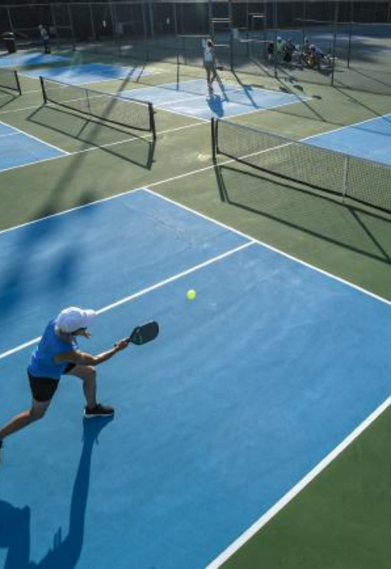 Player hitting pickleball on blue court with multiple courts in the background