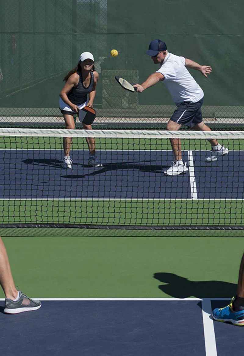 Pickleball doubles match at the net, players hitting ball on blue court