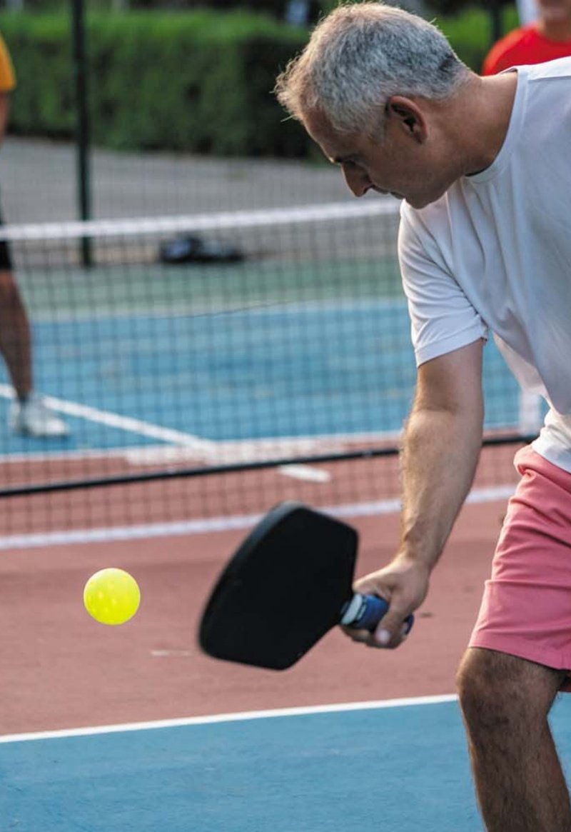 Man playing pickleball, hitting ball with paddle, wearing a white shirt and pink shorts