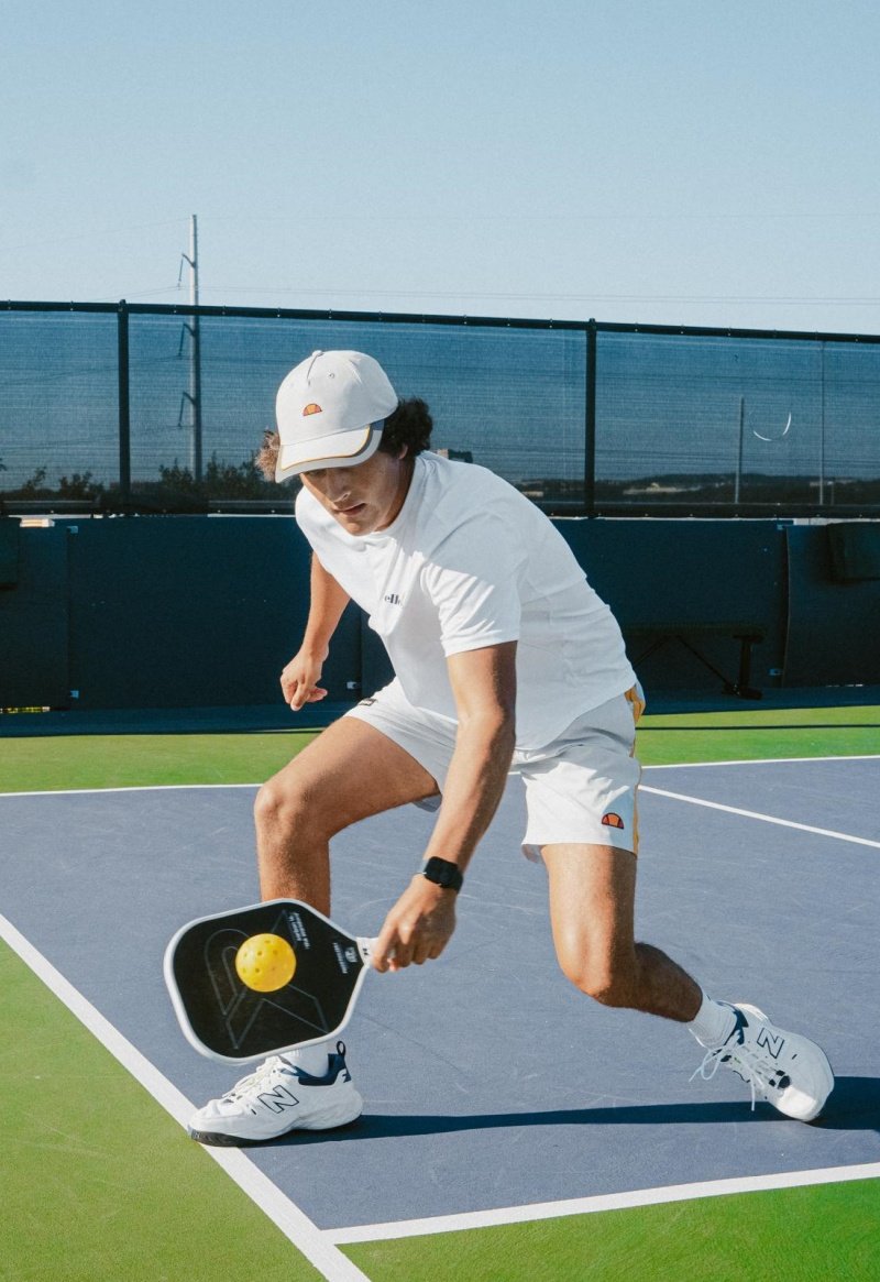 Pickleball player hitting ball on court, wearing a white cap and shirt