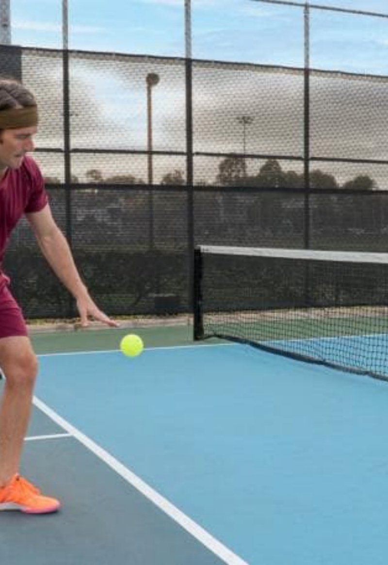pickleball player action man hitting pickleball on court, with green fence and blue court