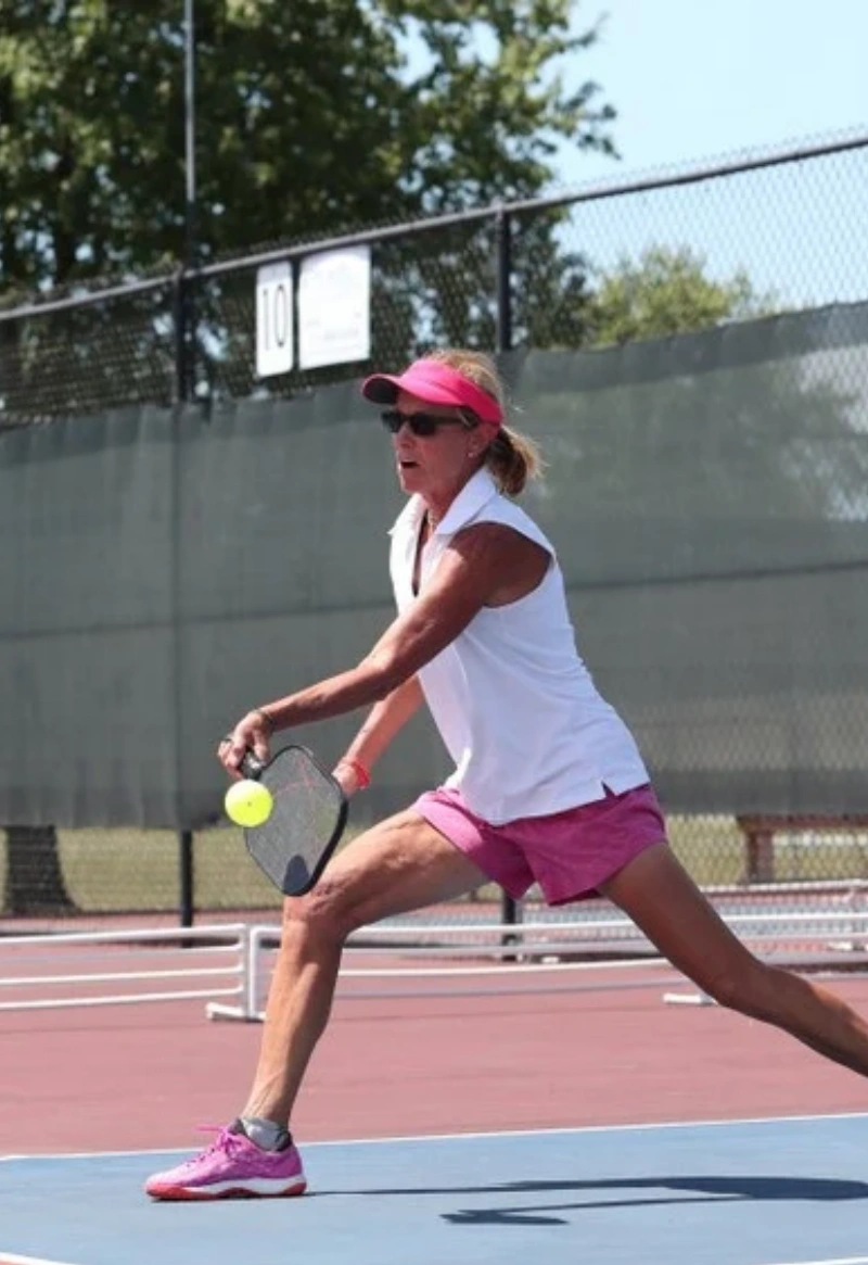 pickleball woman swing female pickleball player hitting ball, with pink outfit and green trees in background