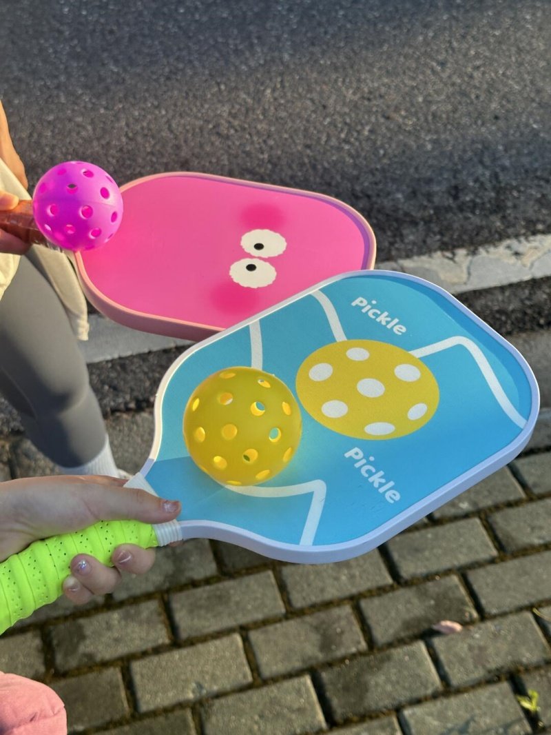 Fun pickleball paddle designs Two colorful pickleball paddles with matching balls in outdoor sunlight