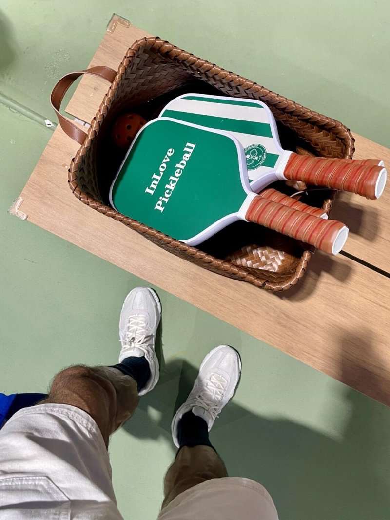 Green pickleball paddles in basket Green pickleball paddles with brown grips in a basket on a wooden bench
