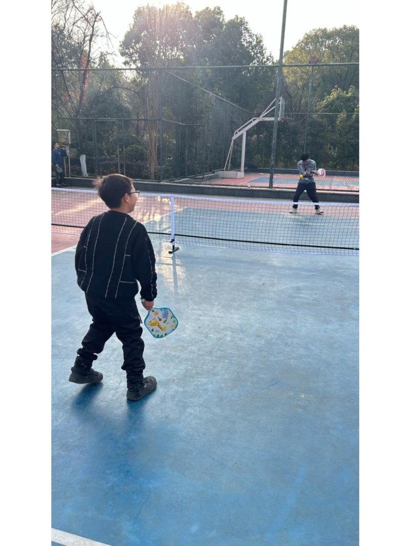 Kids Pickleball Match Two kids playing pickleball on an outdoor court with a blue surface