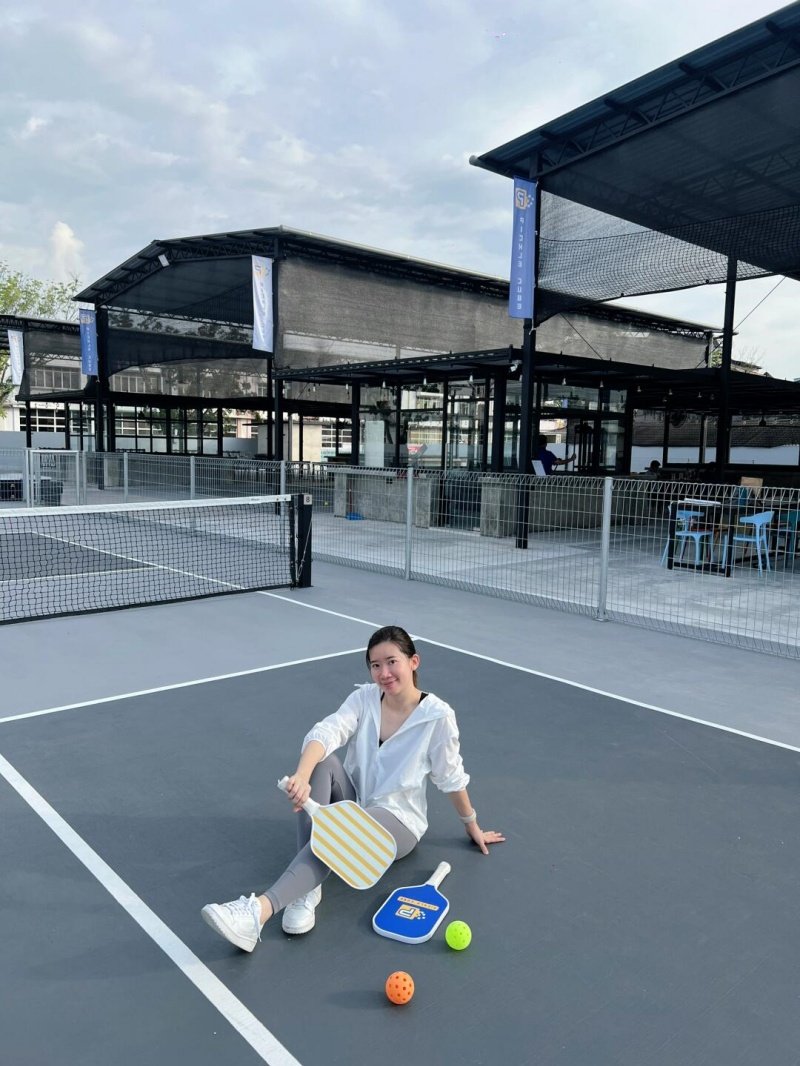 Pickleball Court Break Woman sitting on a grey pickleball court with paddles and balls