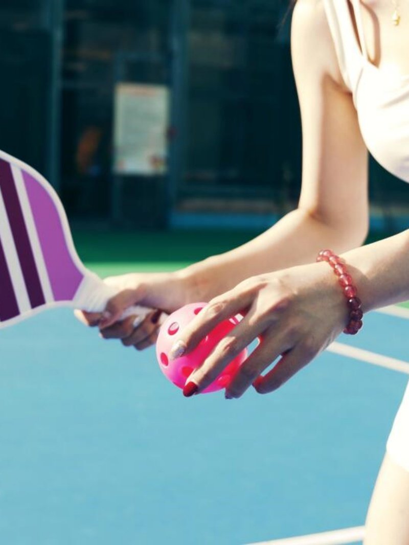 Pickleball Ready to Serve Close-up of a woman holding a pink pickleball and paddle on a blue court