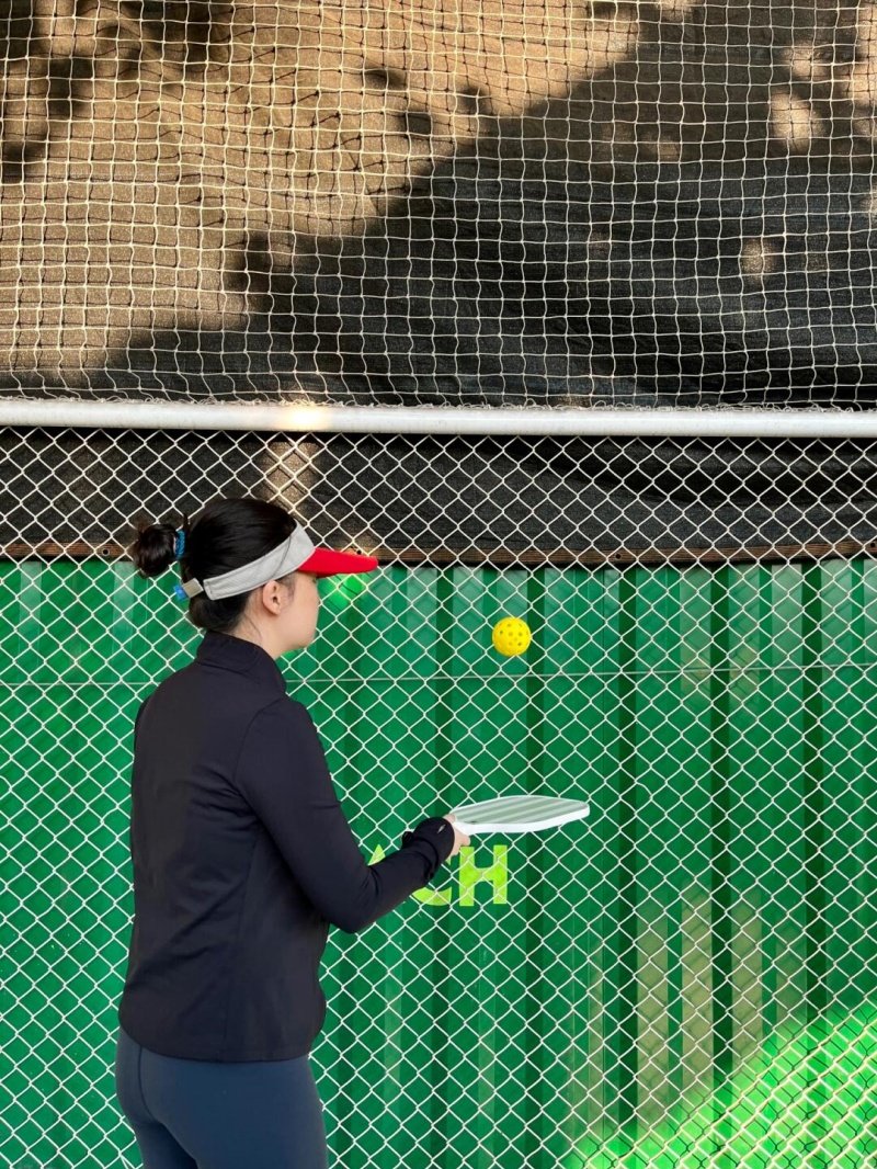 Pickleball Solo Training Woman practicing pickleball against a green fence with a yellow ball