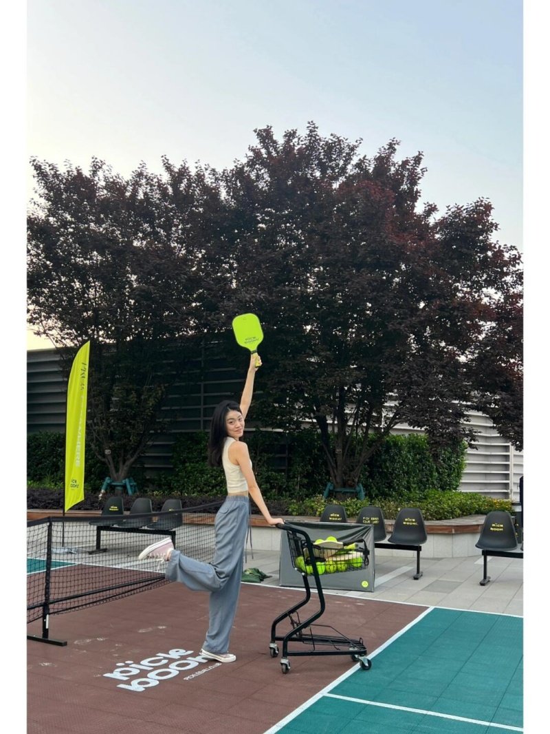 Woman posing on a pickleball court with a bright green paddle