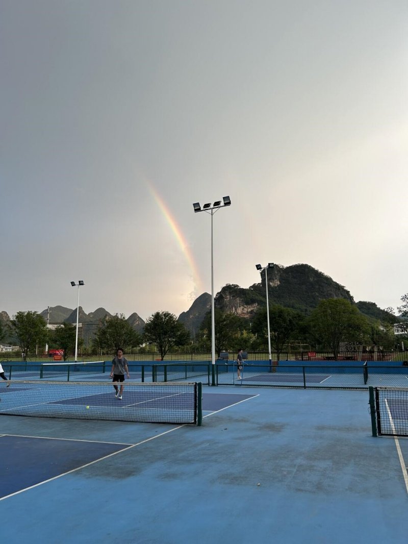 Pickleball courts with scenic rainbow Outdoor pickleball courts with players and a rainbow over mountains