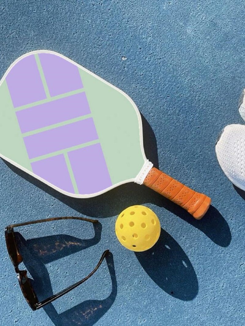 Pickleball essentials in sunlight Pickleball paddle, ball, and sunglasses on blue court