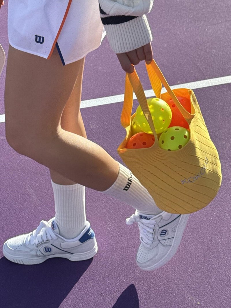 Pickleball gear in motion Pickleball player carrying a yellow bag of balls on a purple court