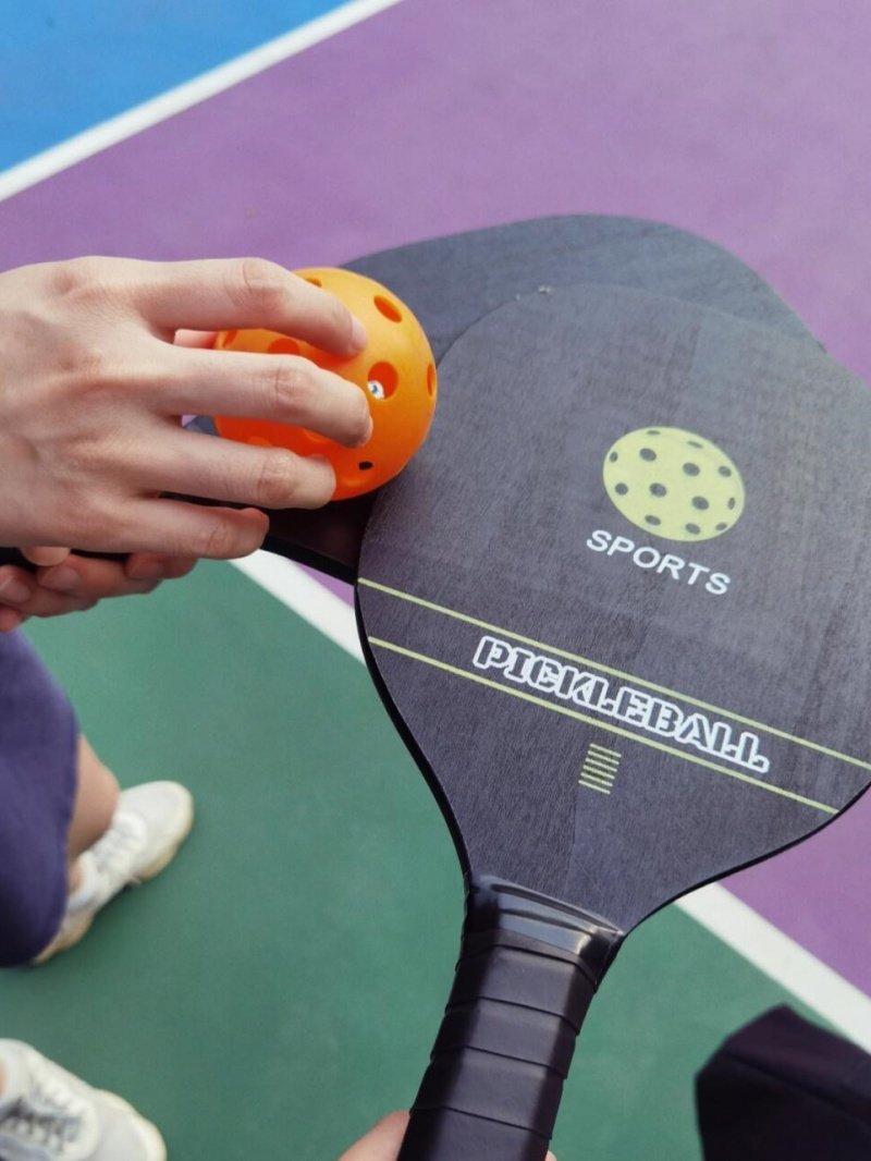 Close-up of pickleball paddles and an orange pickleball on a colorful court