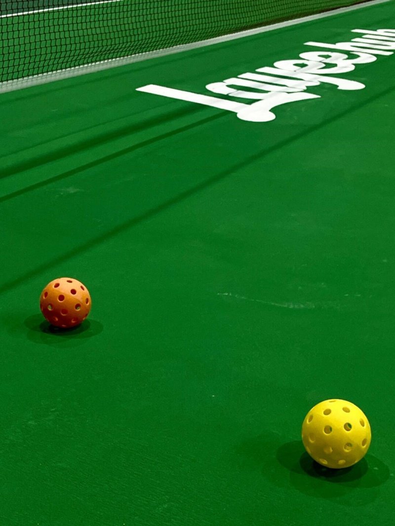 Pickleballs on Court Two pickleballs on a green court, one orange and one yellow
