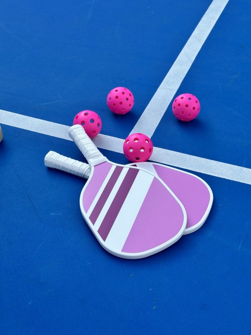 Pink Pickleball Gear on Court Two pink pickleball paddles and four pink balls on a blue court