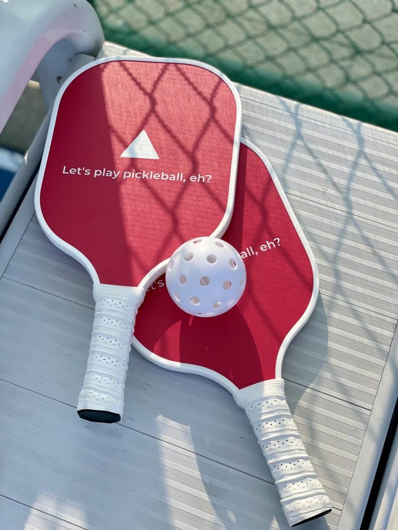 Red pickleball paddles and ball Two red pickleball paddles with white grips and a ball on a bench