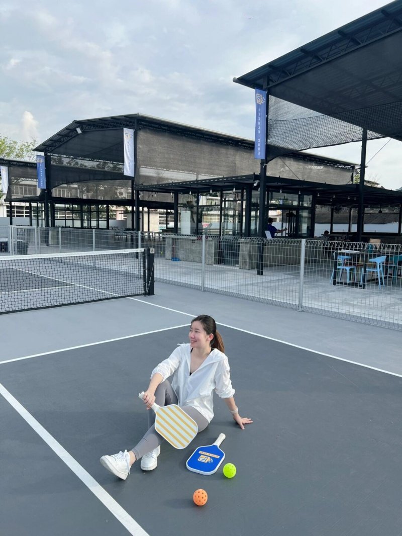 Relaxing on the Pickleball Court Woman sitting on a pickleball court with paddles and balls