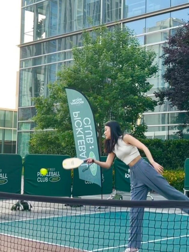 Woman playing pickleball on an outdoor court near modern buildings