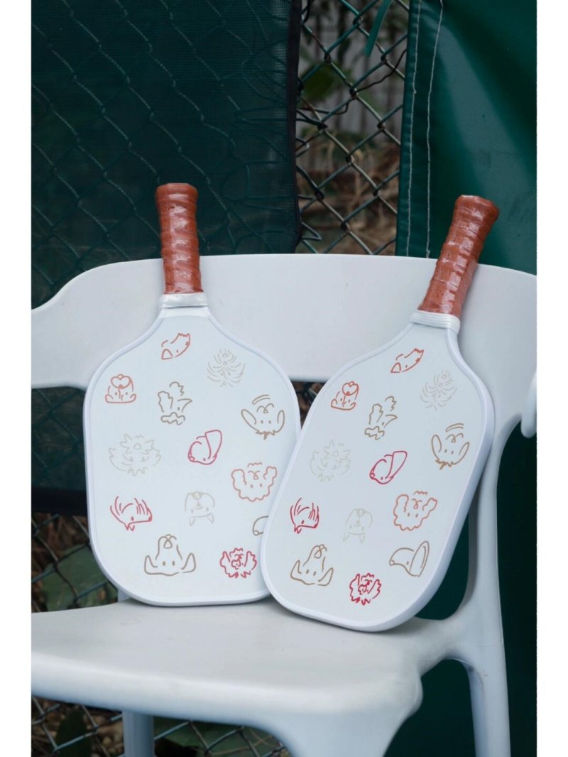 White pickleball paddles with doodles Two white pickleball paddles with brown grips and doodle designs on a chair