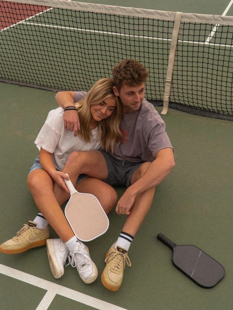 Couple sitting on pickleball court, holding paddles, smiling together