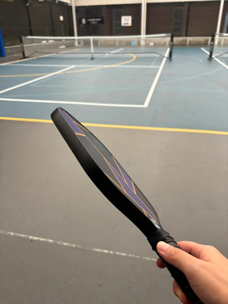 Pickleball paddle with geometric design held in hand, sports court in background