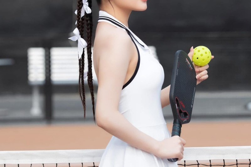 Elegant Pickleball Player Woman in white dress holding carbon pickleball paddle and green ball