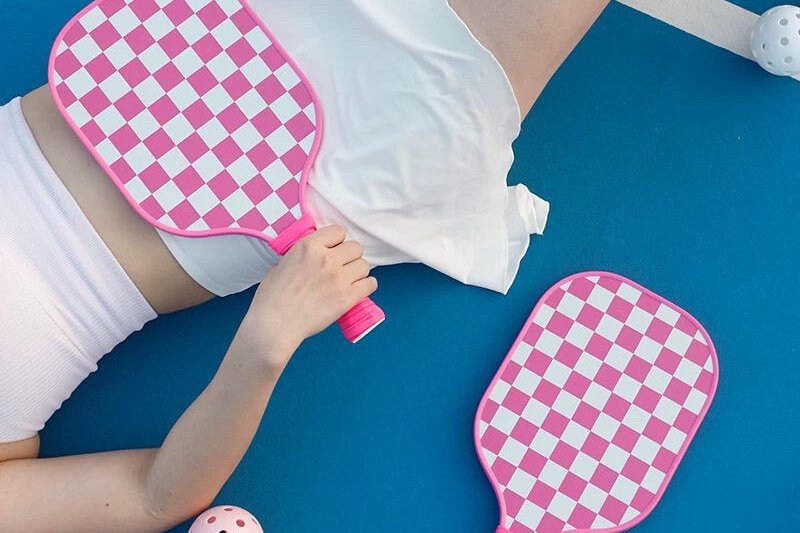 Holding Pink Paddle Person holding pink checkerboard pickleball paddle on blue court