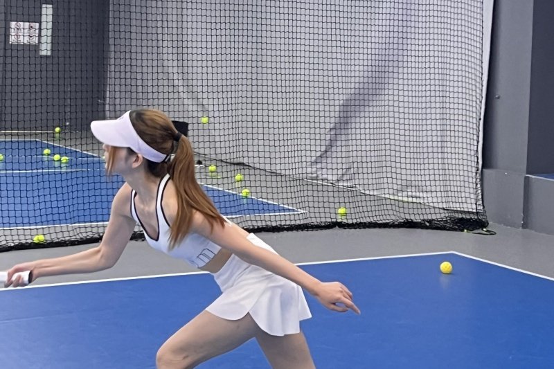 Indoor Court Action Woman in white sports outfit playing indoors on blue court