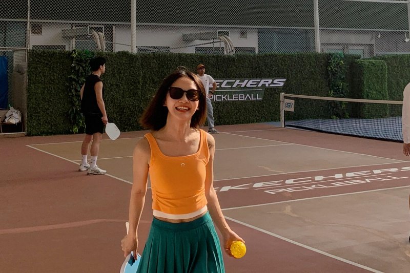 Woman holding paddle and ball on outdoor pickleball court
