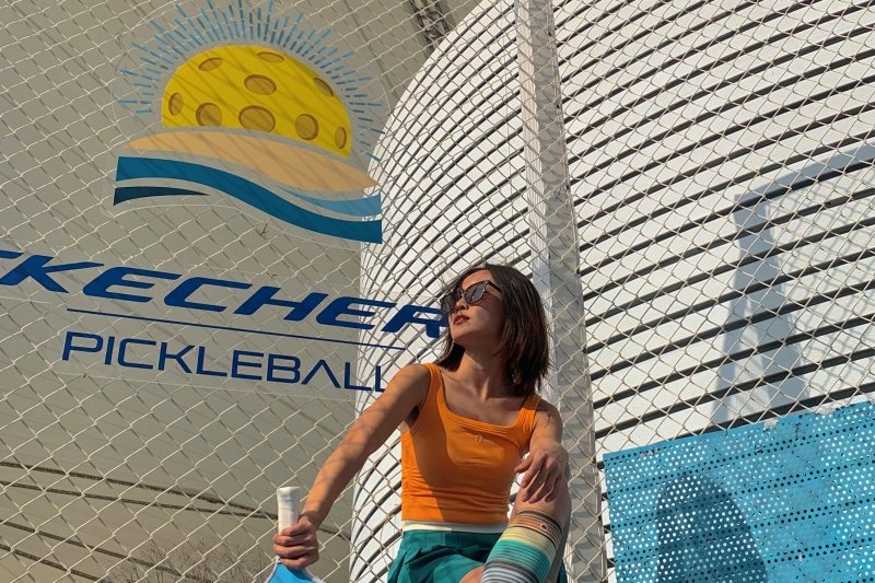 Woman with paddle in front of Skechers Pickleball banner