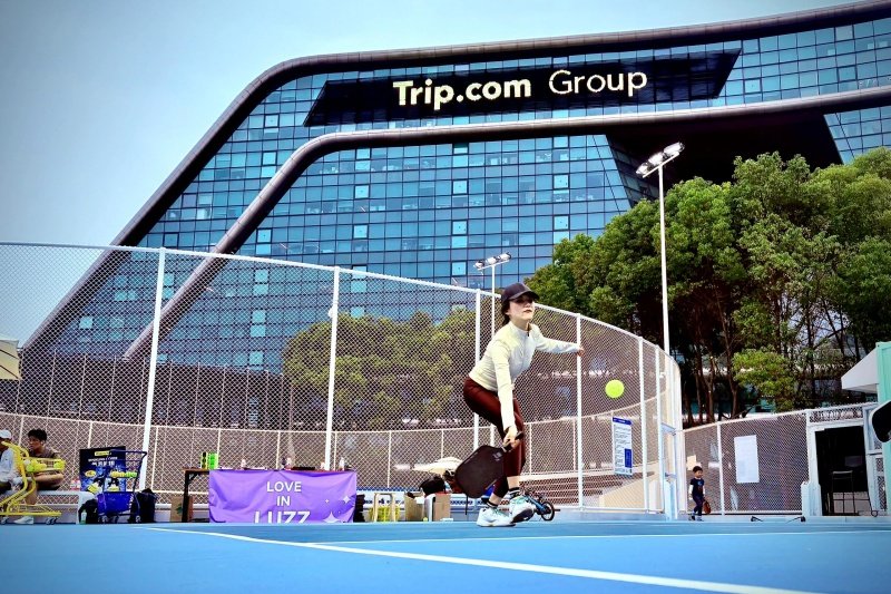 Pickleball serve with skyline Woman serving pickleball with Trip.com building in background