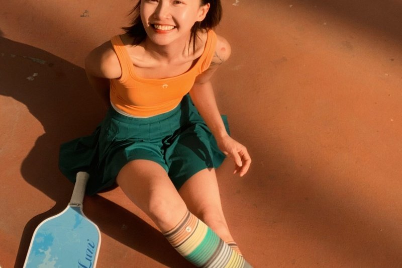 Smiling woman sitting on court with blue pickleball paddle