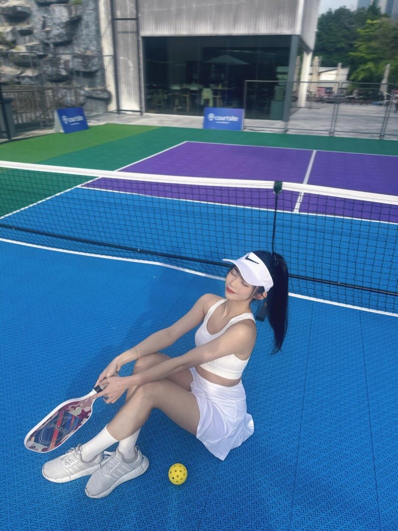 Relaxing Court Moment Woman in white outfit sitting on vibrant pickleball court with paddle and ball