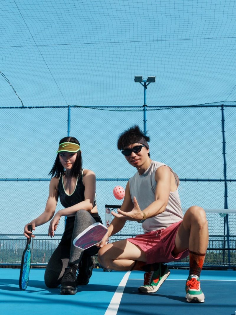 Rooftop Duo Pose Two sporty players pose with paddles on rooftop pickleball court under sunny sky