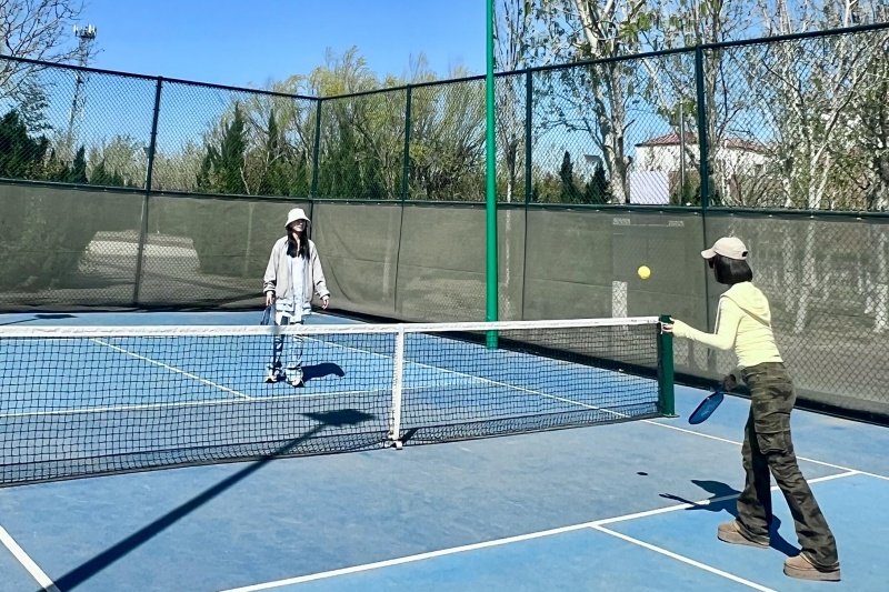 Pickleball Match Two women playing pickleball on blue court with net and paddles